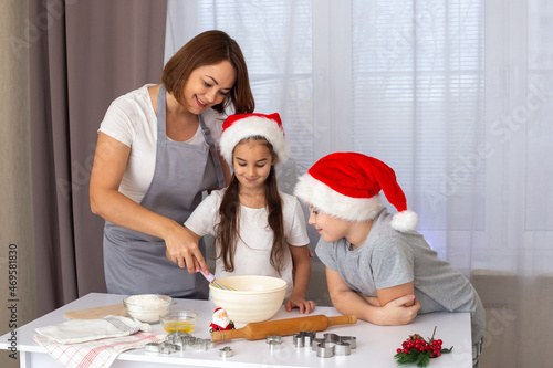 mom and two children in red caps cooking Christmas cookies in the kitchen.