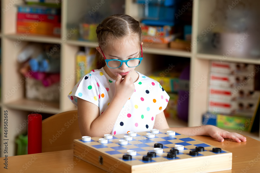 Fototapeta premium Girl with Down Syndrome playing checkers