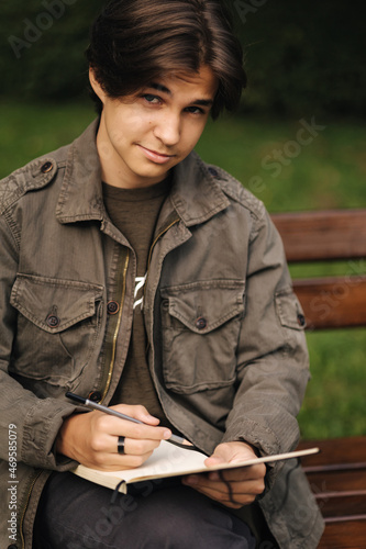 Handsome teenager painting something in his notepad outdood during the break. Talanted young boy photo