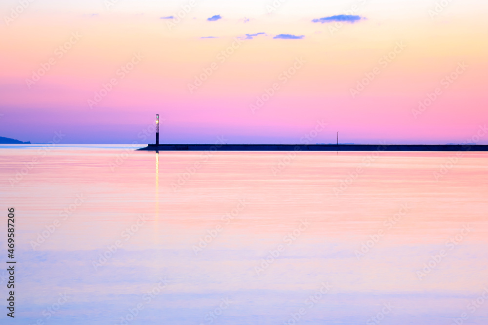 A concrete breakwater on a horizon. A beautiful seascape. Lighthouse in twilight