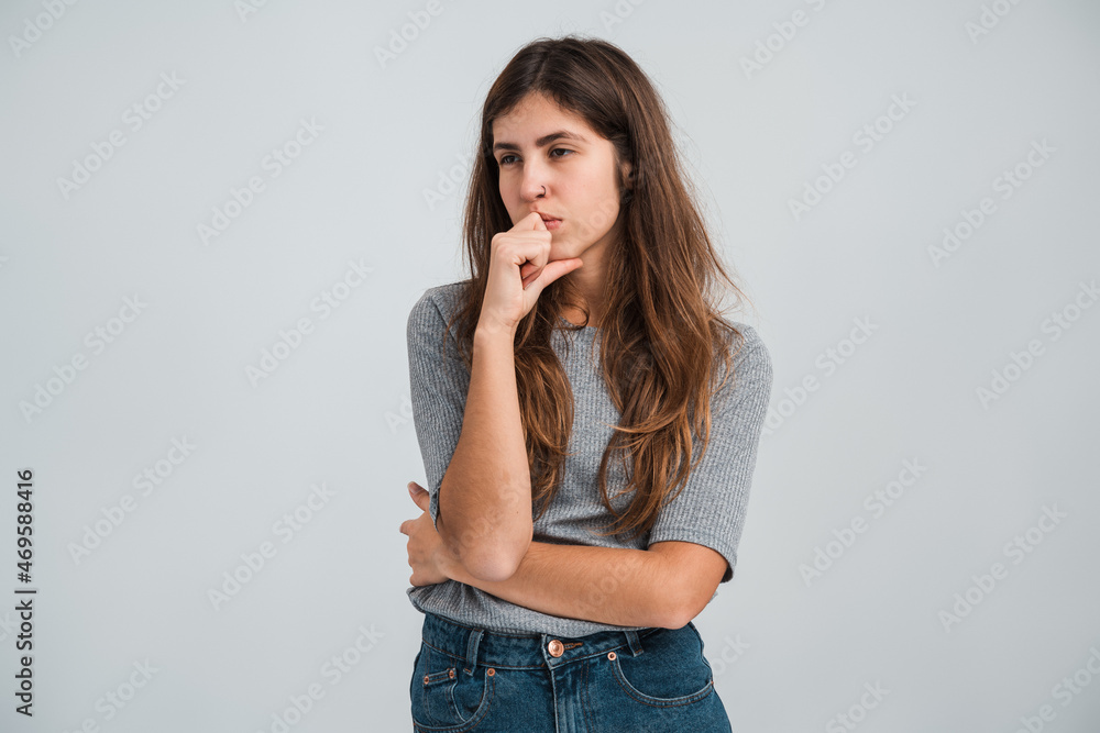 Hmm, lets my think. Pleased, confusion concept. Woman in casual clothes looking away, touching chin and thinking. Studio shot