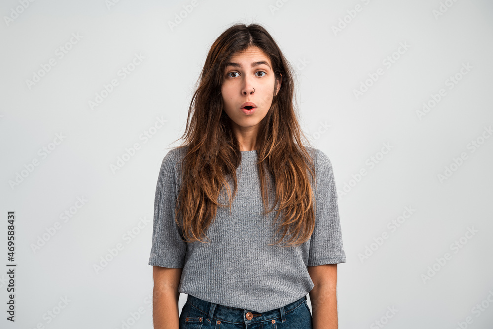 Front view of astonished woman in casual sweater standing with mouth open in surprise, having shocked expression, hearing unbelievable news. Indoor studio shot isolated on white background Front view of astonished woman in casual sweater standing with mouth open in surprise, having shocked expression, hearing unbelievable news. Indoor studio shot isolated on white background