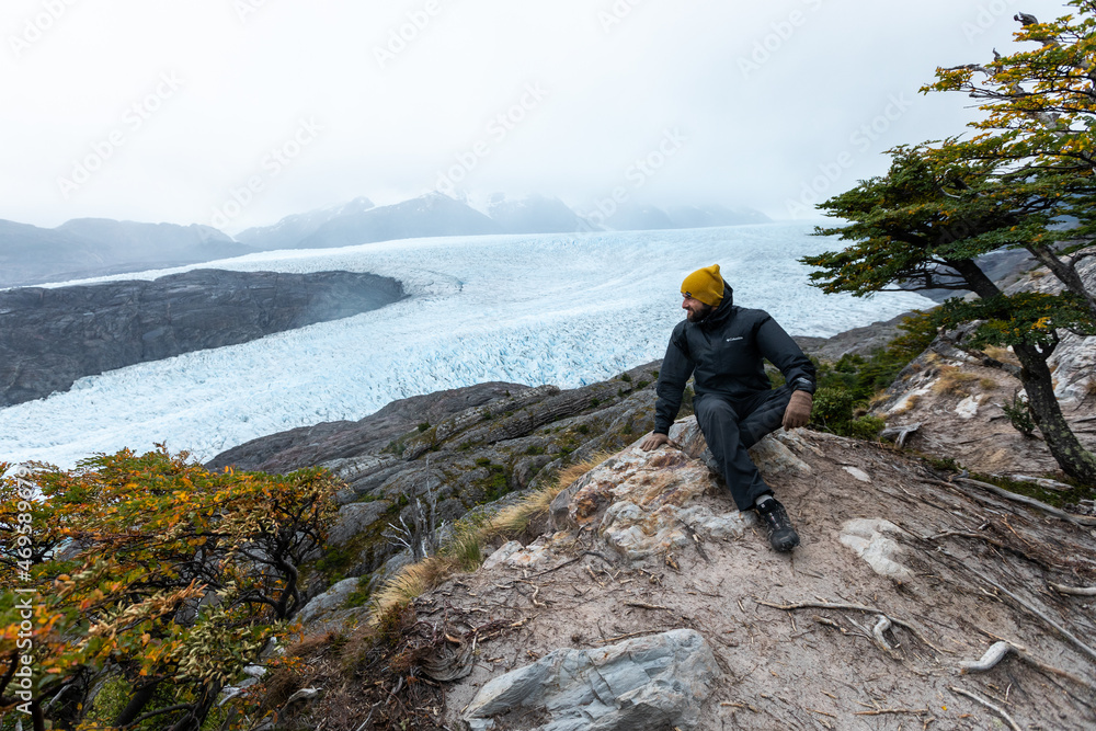 Obraz premium A young man sits on the rock with Grey Glacier on the background, Torres del Paine National Park, Chile