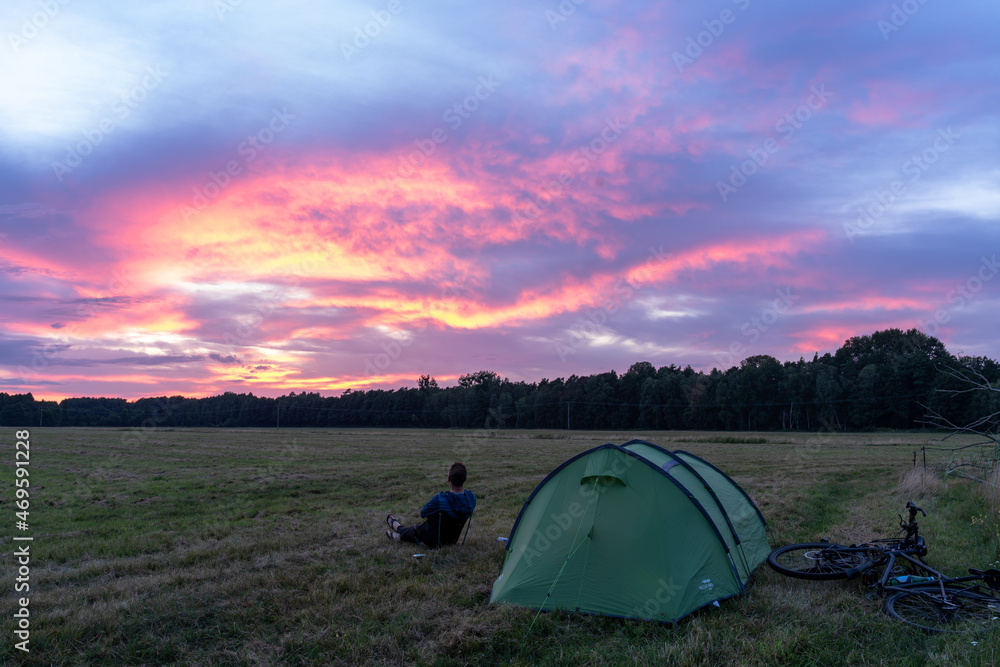 Person sitting in front of tent in field during a pink sunset, Grabow, Germany