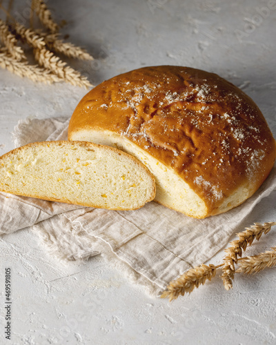 Loaf of round fresh homemade white bread with some slices cut isolated with wheat spikelets