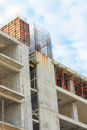 Concrete construction of a new high-rise apartment building. An unfinished buildings facade view from outside. Residential complex exterior. Real estate. Slabs, walls, metal rods. Vertical photography