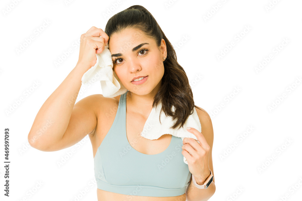 Gorgeous woman sweating and using a gym towel after finishing working out. Sporty woman exercising and making eye contact Gorgeous woman sweating and using a gym towel after finishing working out. Sporty woman exercising and making eye contact