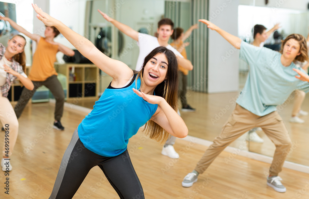 Obraz premium Happy brunette teenage girl dancer practicing active vigorous dance with group in modern studio.