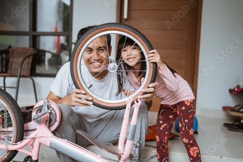 Smiling father and daughter looking at camera between bicycle wheels