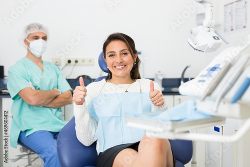 Young satisfied woman smiling with white teeth showing thumbs up at dental clinic office