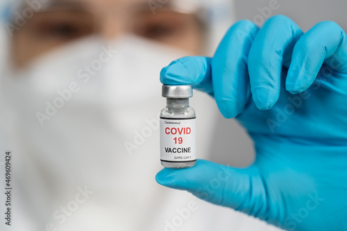 doctor in PPE suit holding and gently shaking Coronavirus (Covid-19) vaccine bottle