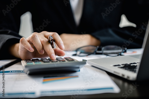 Close up of Businesswomen or Accountant using a calculator and laptop computer with analytic business report graph and finance chart at the workplace  financial and investment concept.