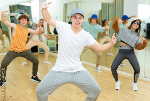 Portrait of expressive teenage krump dancer in choreographic studio with dancing teenagers in background. Typical Generation Z .