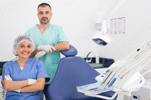 Portrait of a young attractive dentist and his female assistant in uniform with crossed hands near medical chair photo