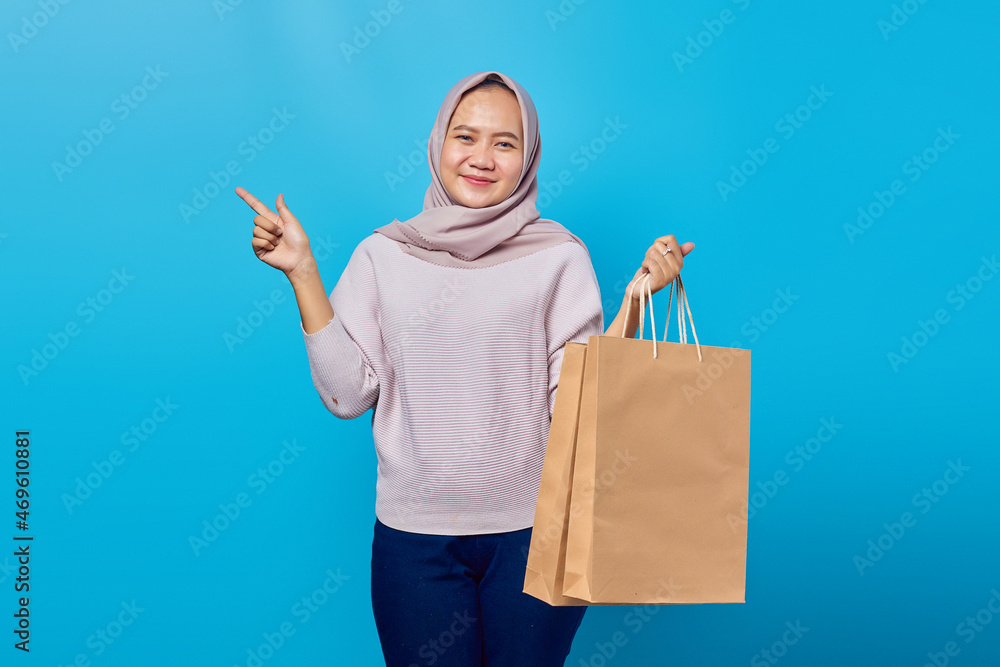 Portrait of cheerful asian woman holding shopping bag and pointing finger at empty space Portrait of cheerful asian woman holding shopping bag and pointing finger at empty space