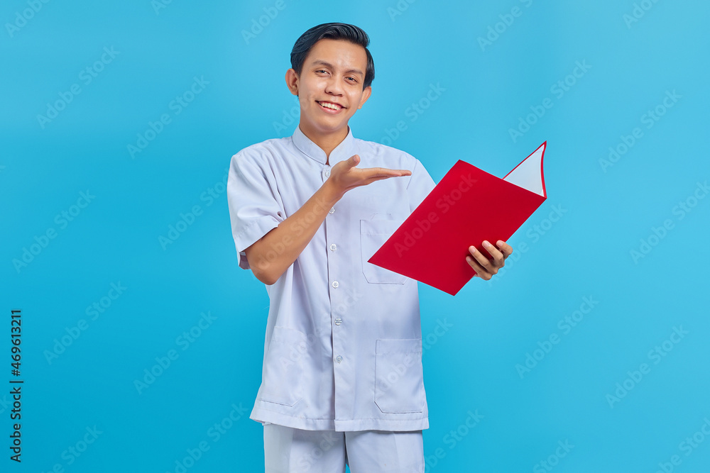 Portrait of smiling male nurse pointing at folder with palms over blue background Portrait of smiling male nurse pointing at folder with palms over blue background