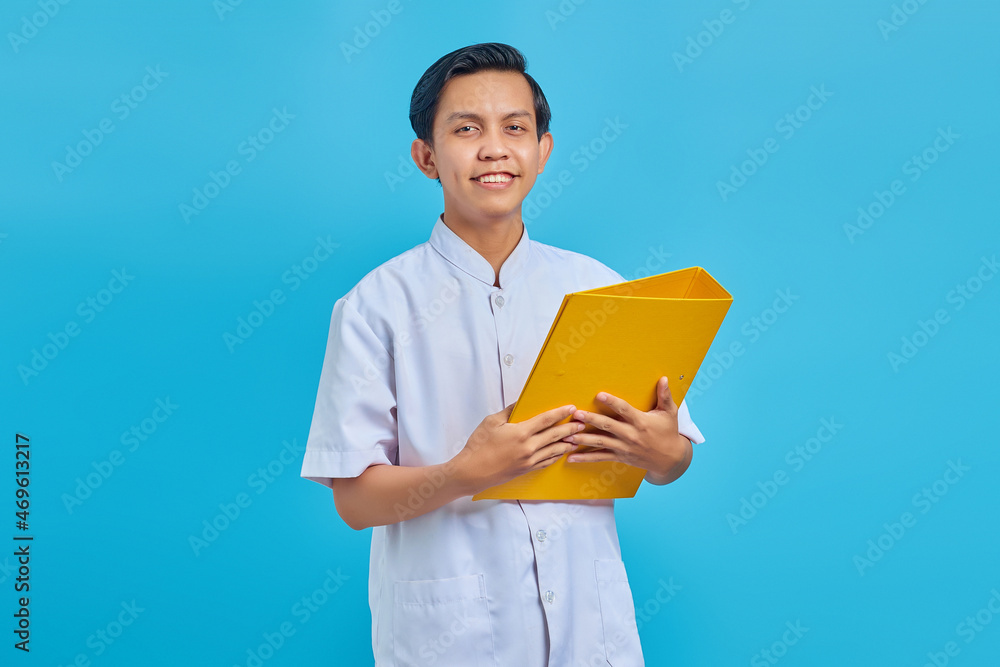 Portrait of cheerful male nurse holding yellow folder on blue background Portrait of cheerful male nurse holding yellow folder on blue background