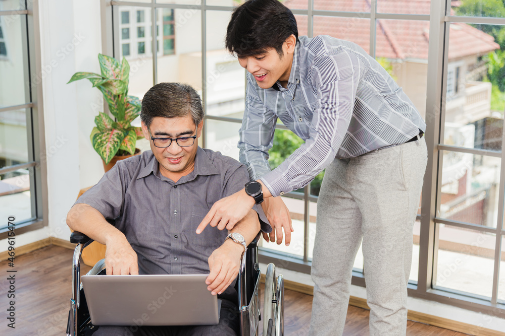 Fototapeta premium Asian senior disabled businessman in a wheelchair with laptop computer discuss together with team in office. Old father man sitting wheelchair and his son talking video calls conference on laptop