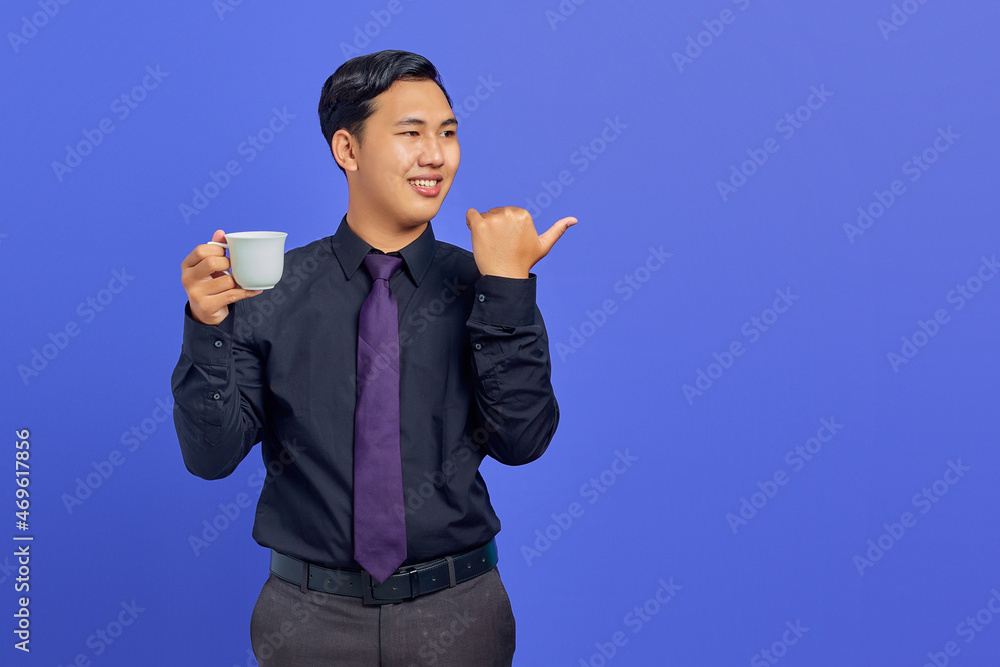 Photo of smiling handsome businessman holding cup and pointing aside on purple background Photo of smiling handsome businessman holding cup and pointing aside on purple background