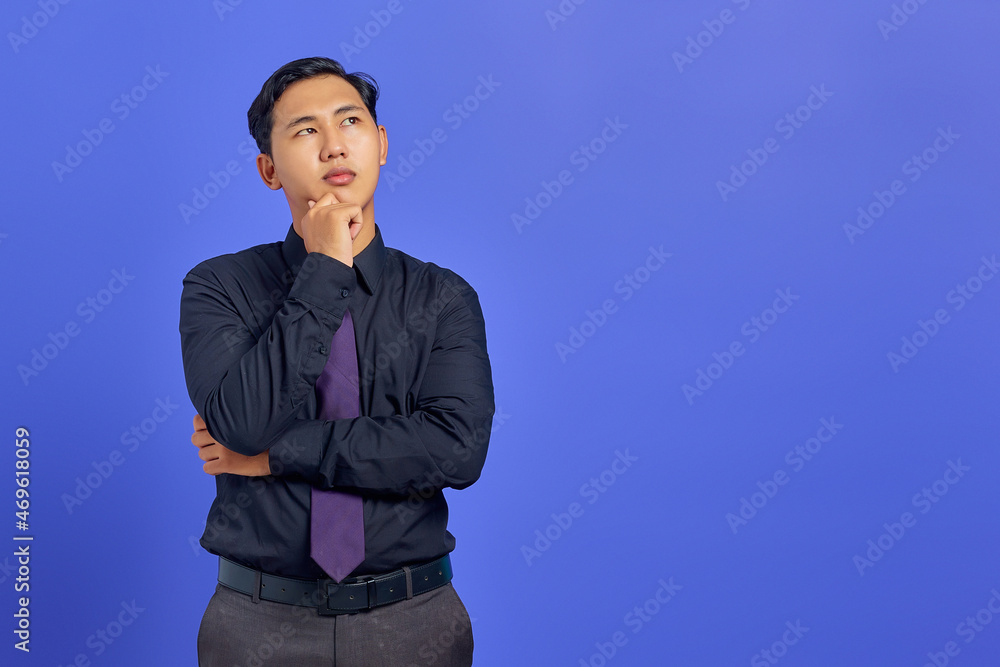 Pensive young handsome businessman rubs chin and thinking about a question on purple background Pensive young handsome businessman rubs chin and thinking about a question on purple background