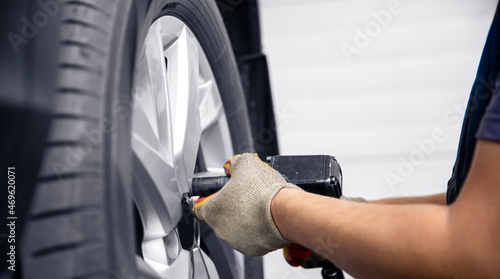 Concept car service replacement of winter and summer tires. Mechanic unscrews wheel bolts from red auto © Parilov