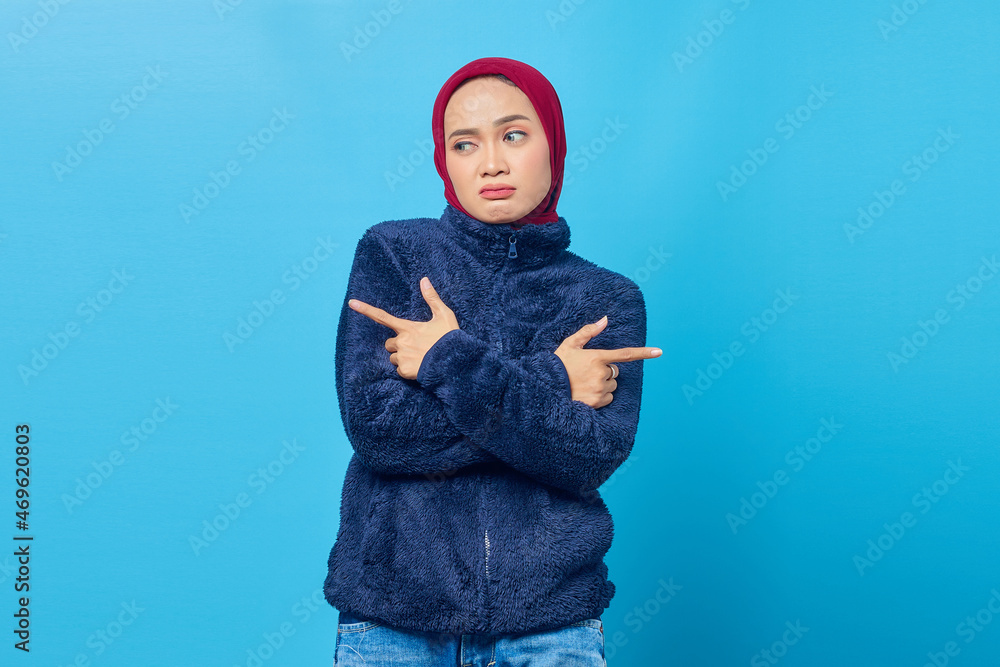 Confused young Asian woman pointing sideways and looking sideways on blue background