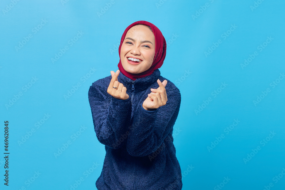 Cheerful young Asian woman showing heart sign with fingers crossed on blue background Cheerful young Asian woman showing heart sign with fingers crossed on blue background
