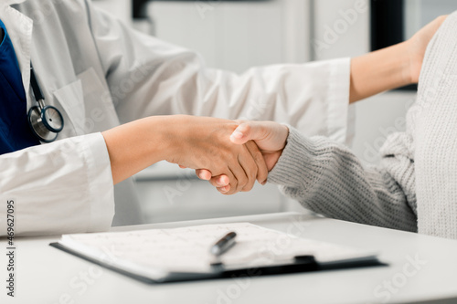 Close up of female Doctor and patient shaking hands after discussing and consulting with a patient in an examination room at a hospital, Medical and Health Care Concept.