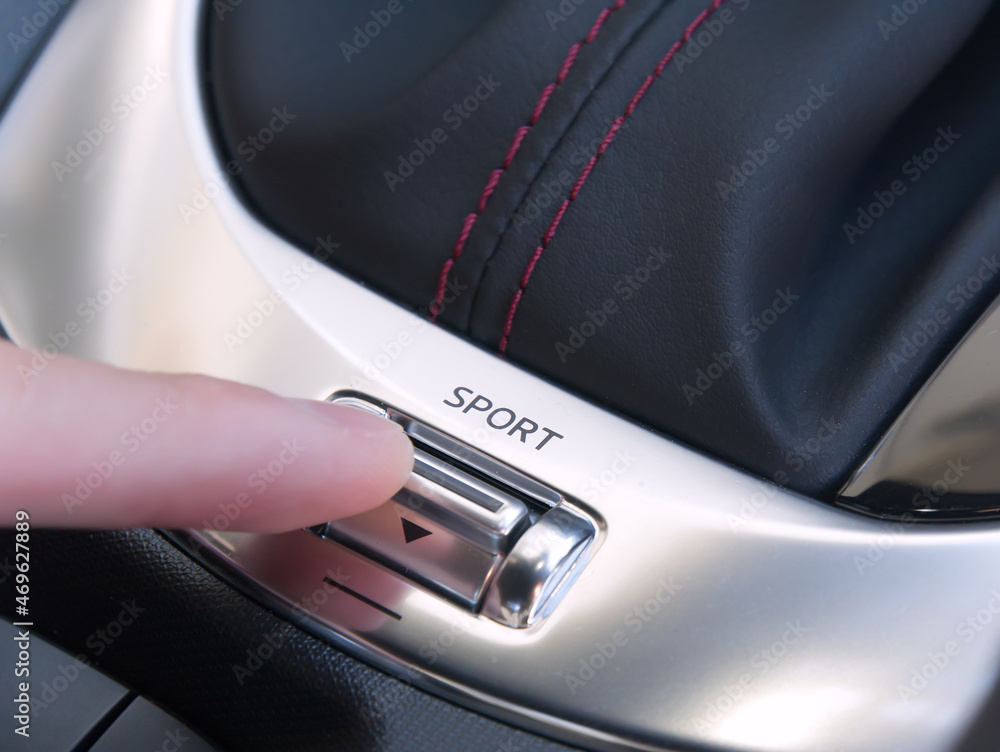車の走行モード切り替えスイッチを指で押して、スポーツモードをONにする（Person operating the car's driving mode switch with finger, sports mode ON）