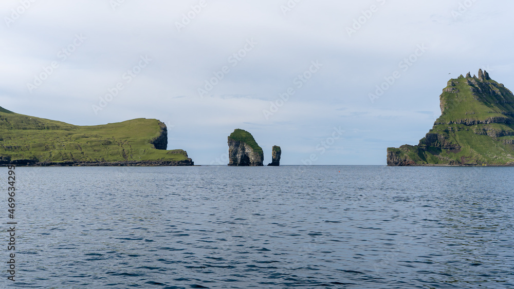 View of the impressive Rocky Drangarnir sea stack and the fishing farms in the Faroe Islands seen from the ferry to Mykines 