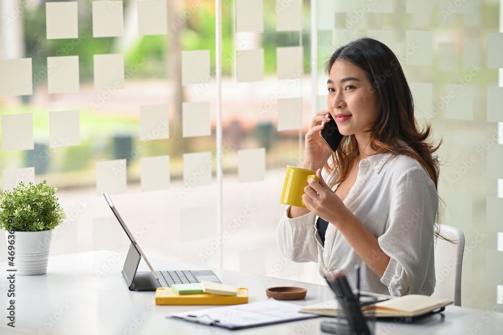 Businesswoman sits in a modern office, sipping hot tea while on the phone. Businesswoman sits in a modern office, sipping hot tea while on the phone.