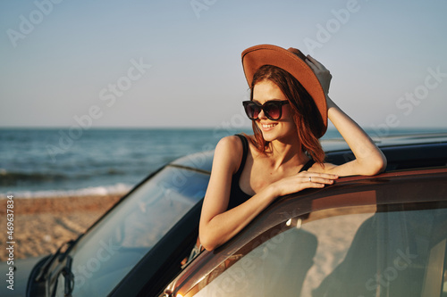 cheerful woman in sunglasses and a hat on the ocean near the car © VICHIZH