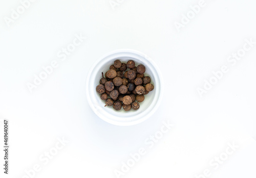 Whole dried black peppercorns in round white bowl on a white background. High quality photo