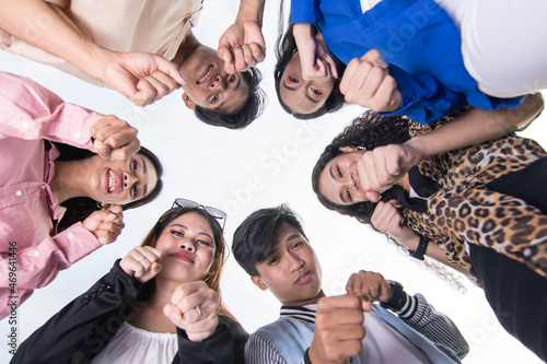 Tablou pe pânză Six young asian friends huddle together, looking down and making a fight gesture with their clenched fist