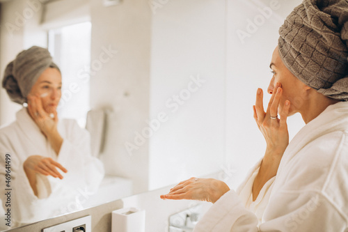 Young woman applying face cream by the mirror