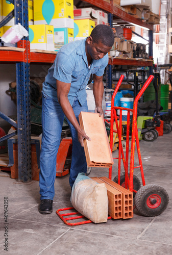 Serious diligent positive friendly African American putting construction supplies on handcart in building hypermarket
