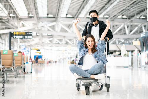 New Normal and travel bubble concept.happy attractive Young Asian tourist couple excited together for the trip female sitting and cheering on baggage trolley or luggage trolley in airport