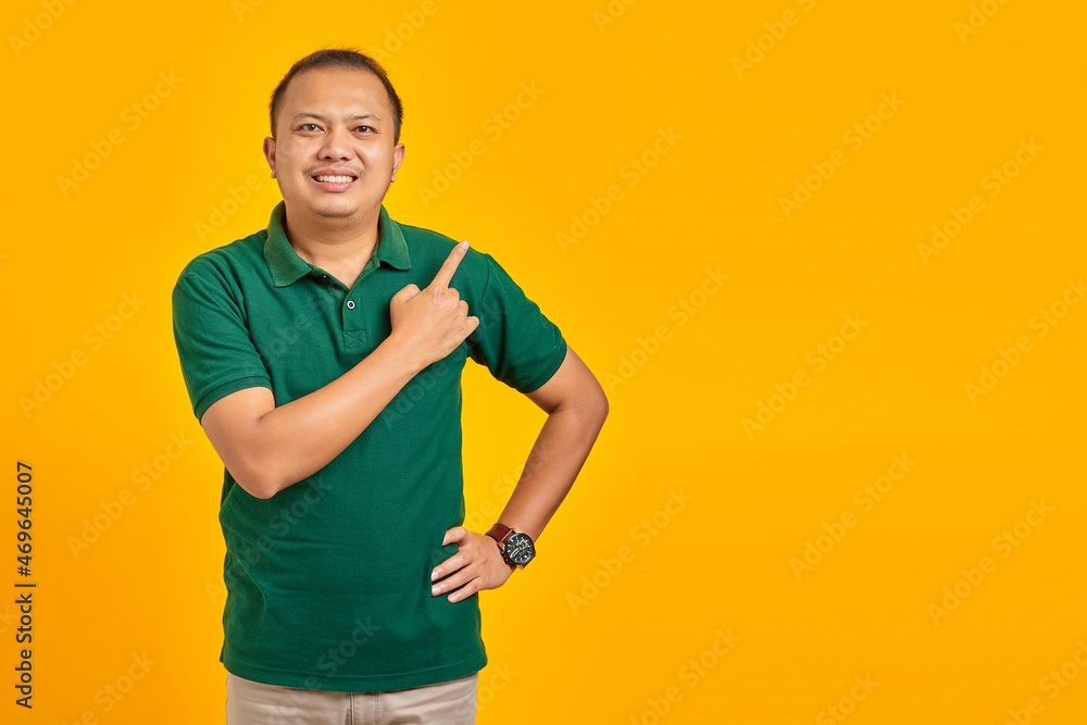 Portrait of smiling young Asian man pointing finger at copy space on yellow background Portrait of smiling young Asian man pointing finger at copy space on yellow background