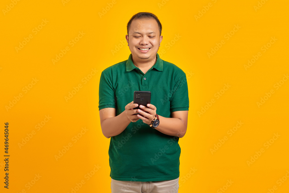 Portrait of cheerful young Asian man using a mobile phone on yellow background Portrait of cheerful young Asian man using a mobile phone on yellow background