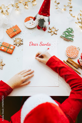 cute little boy in red sweater and Santa hat writes letter to Santa Claus asking to bring presents, top view, New Year and Christmas concept, DIY child, kid believes in miracles © klavdiyav