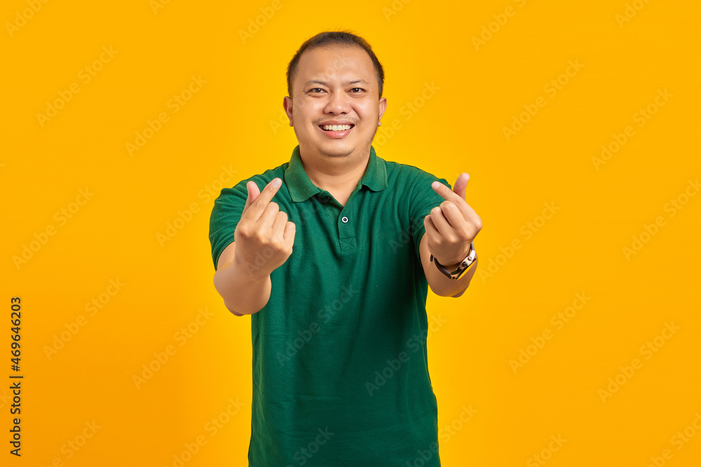 Portrait of cheerful young Asian man showing finger heart over yellow background Portrait of cheerful young Asian man showing finger heart over yellow background