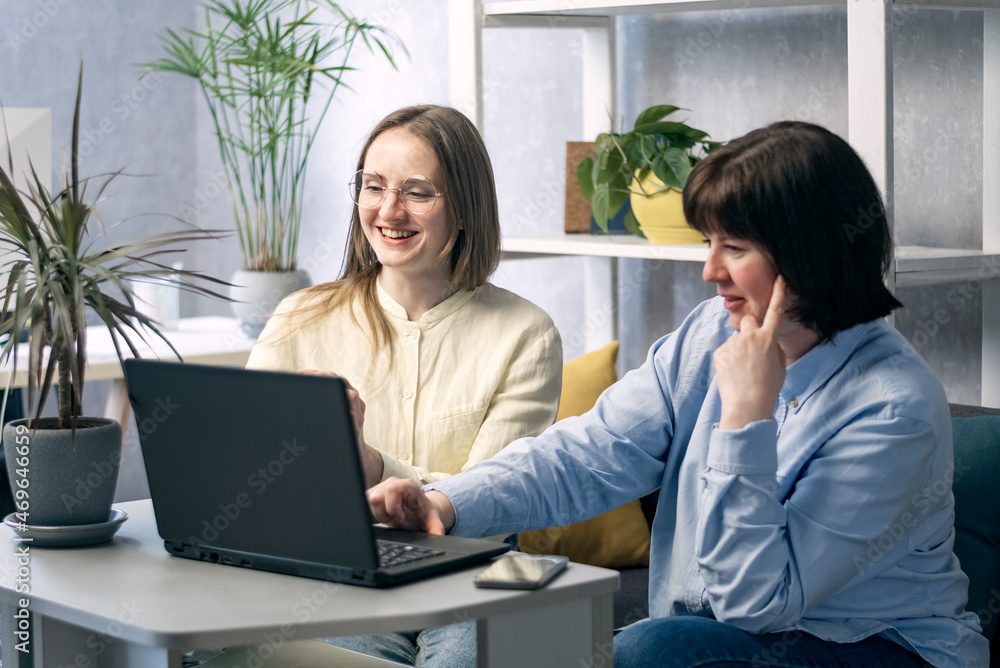 Two young women with laptop are discussing project at work place. Business partners are discussing joint work. Two young women with laptop are discussing project at work place. Business partners are discussing joint work.