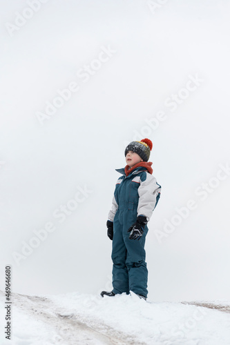 Boy plays outside during snowfall. Winter holidays. Child walks outdoors in winter.
