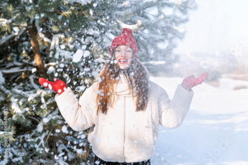 Happy young woman has fun in winter in park. Brunette girl throws snow and laughs.