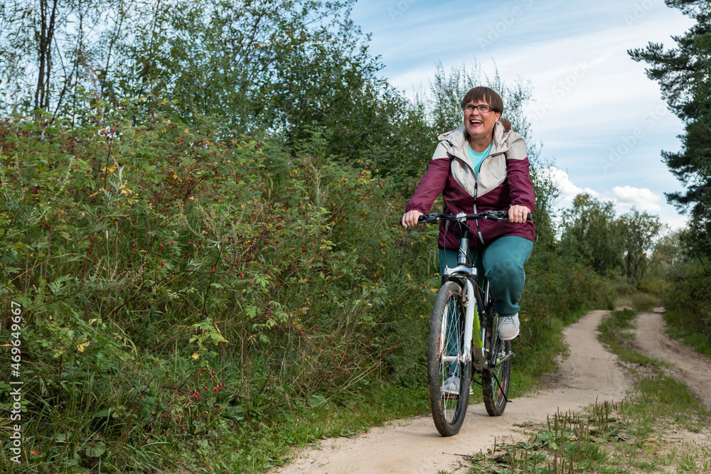 Cheerful grandmother rides a bicycle in nature.