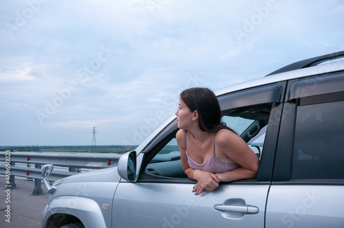 A girl with long hair leaned out of the cab of a car on the road, the concept of auto travel