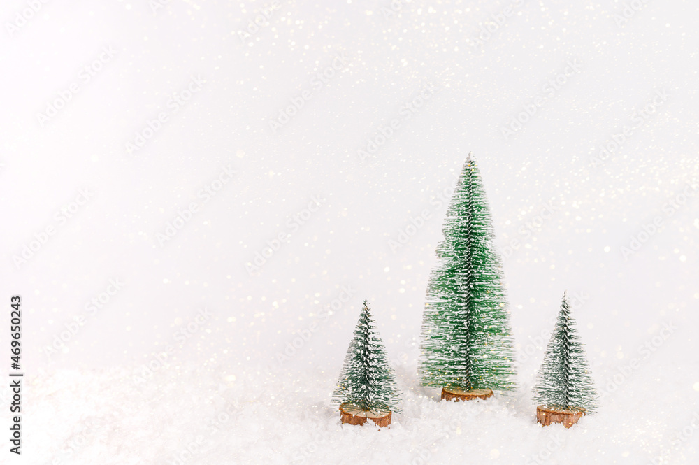 Miniature christmas trees on background with white snow. New year concept. Copy space, front view