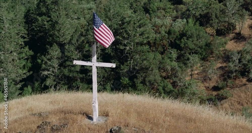 aerial of Wooden cross with american flag waving from it on top of a hill photo
