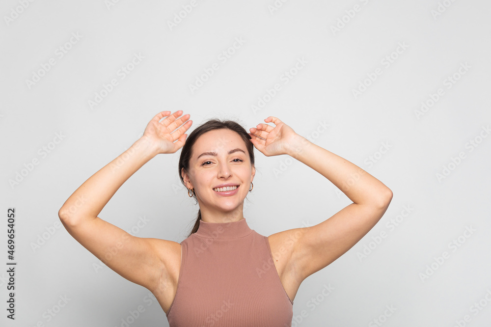 Young woman overjoyed with two hands raised and celebrating victory while standing on grey background copy space