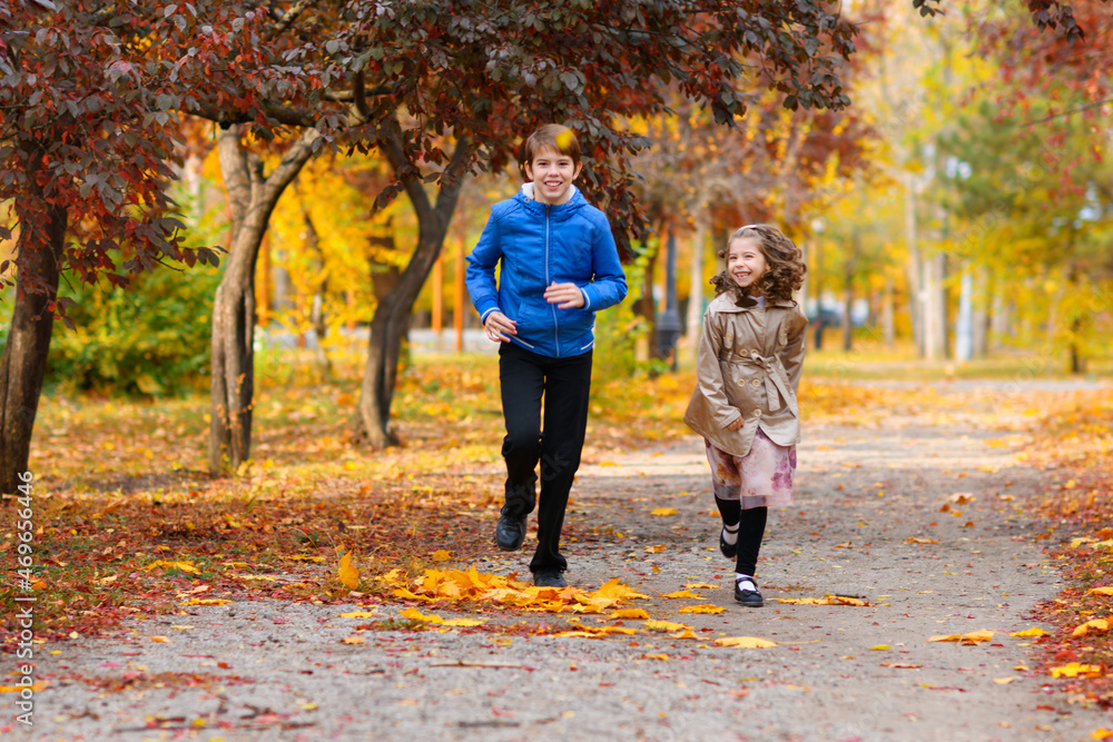 Obraz premium children run along the path in the autumn park . they play and laugh, they have a lot of fun. they are surrounded by beautiful nature and trees with yellow and red leaves